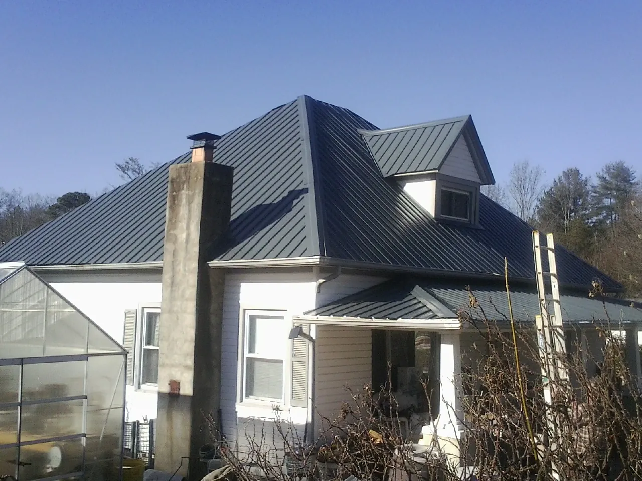 Dark blue standing seam metal roof on a white farmhouse with dormer — Slate & Tile Roof Repair by Roofing Brothers in Connelly