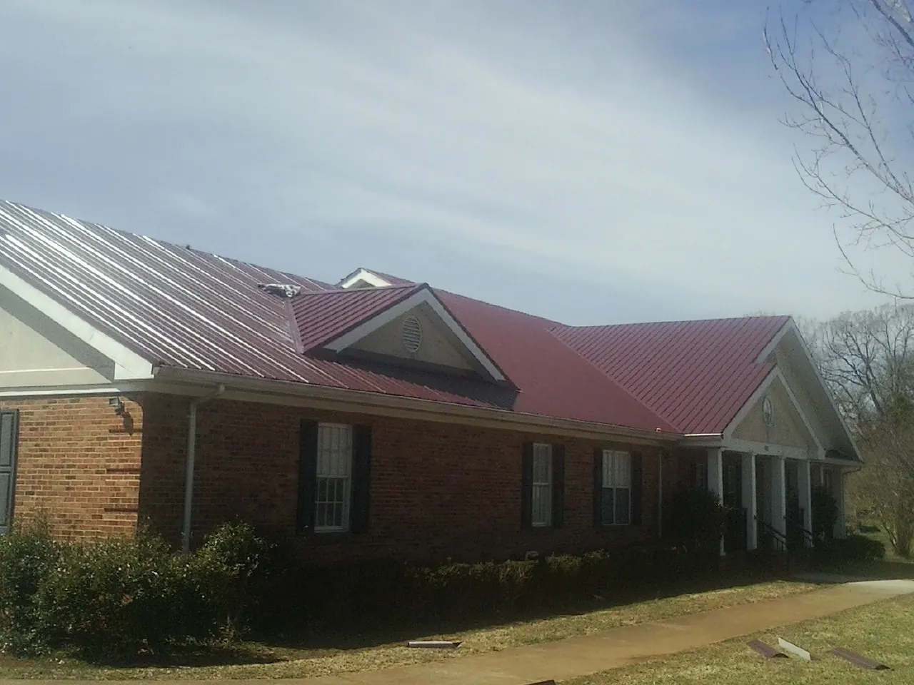 Red metal roof with gabled entries on a long brick building, from a Hail Damage Roof Repair job in Connelly
