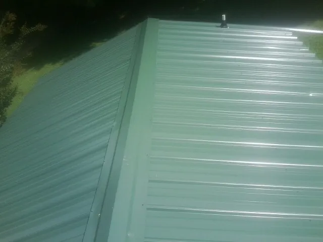 New green metal panels meeting at the ridge of a roof — Flat Roof Repair work by our crew in Connelly