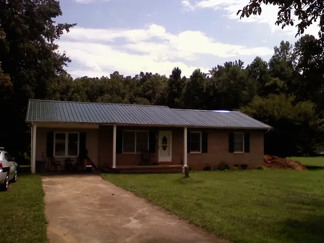 Dark green metal roof on a brick ranch with a covered porch in Connelly