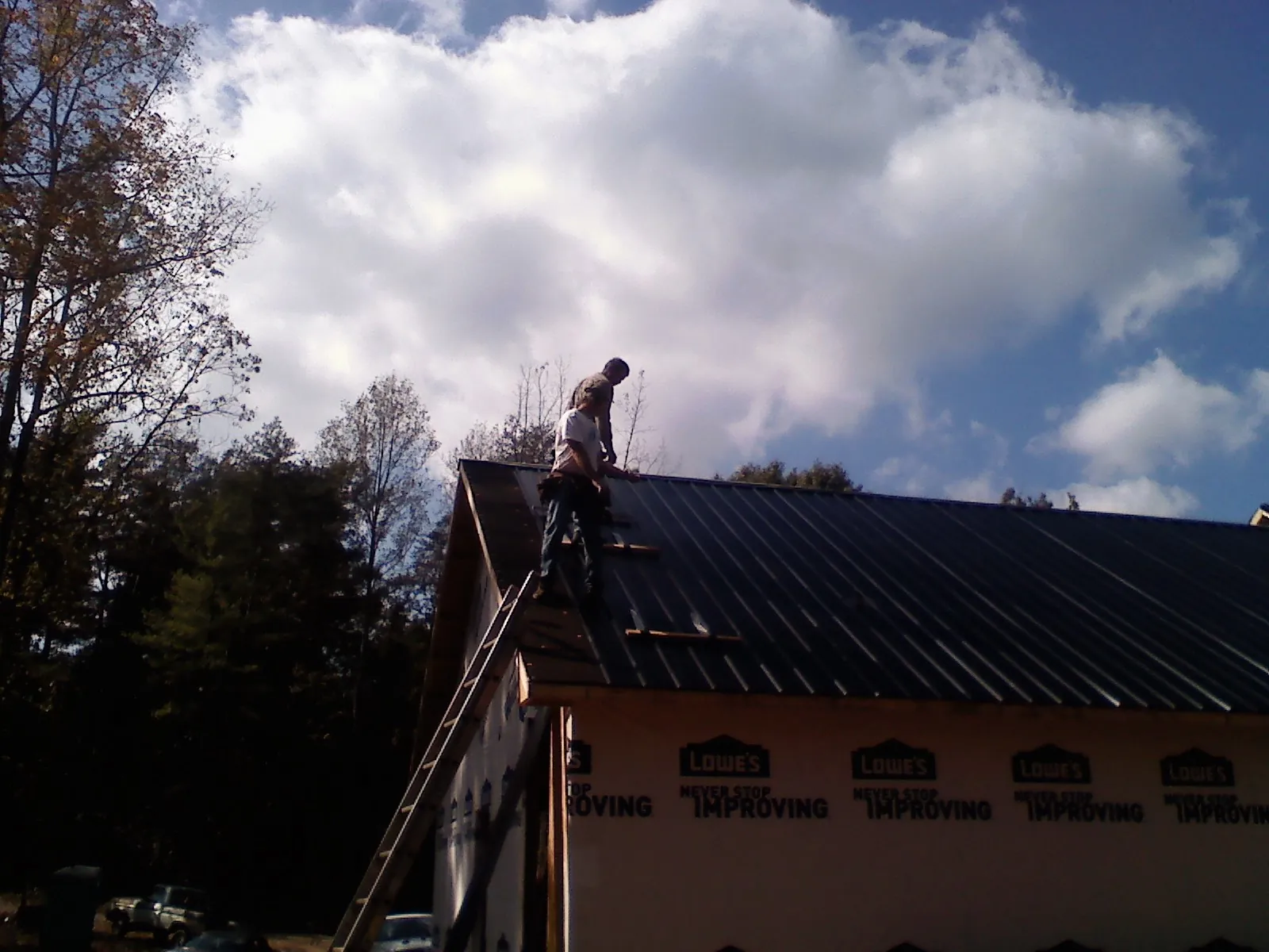 Roofer fastening dark metal panels high against a cloudy sky, from a Roof Inspection job in Connelly