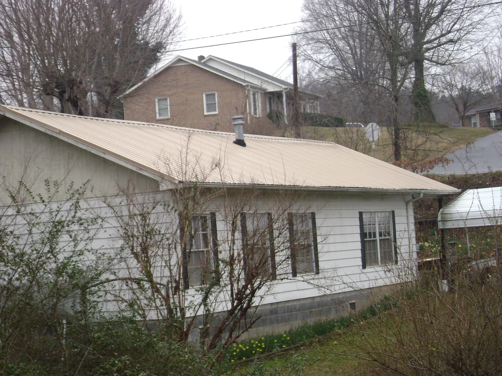 Tan metal roof on a white sided house set into a hillside — Commercial Roofing by Roofing Brothers in Connelly