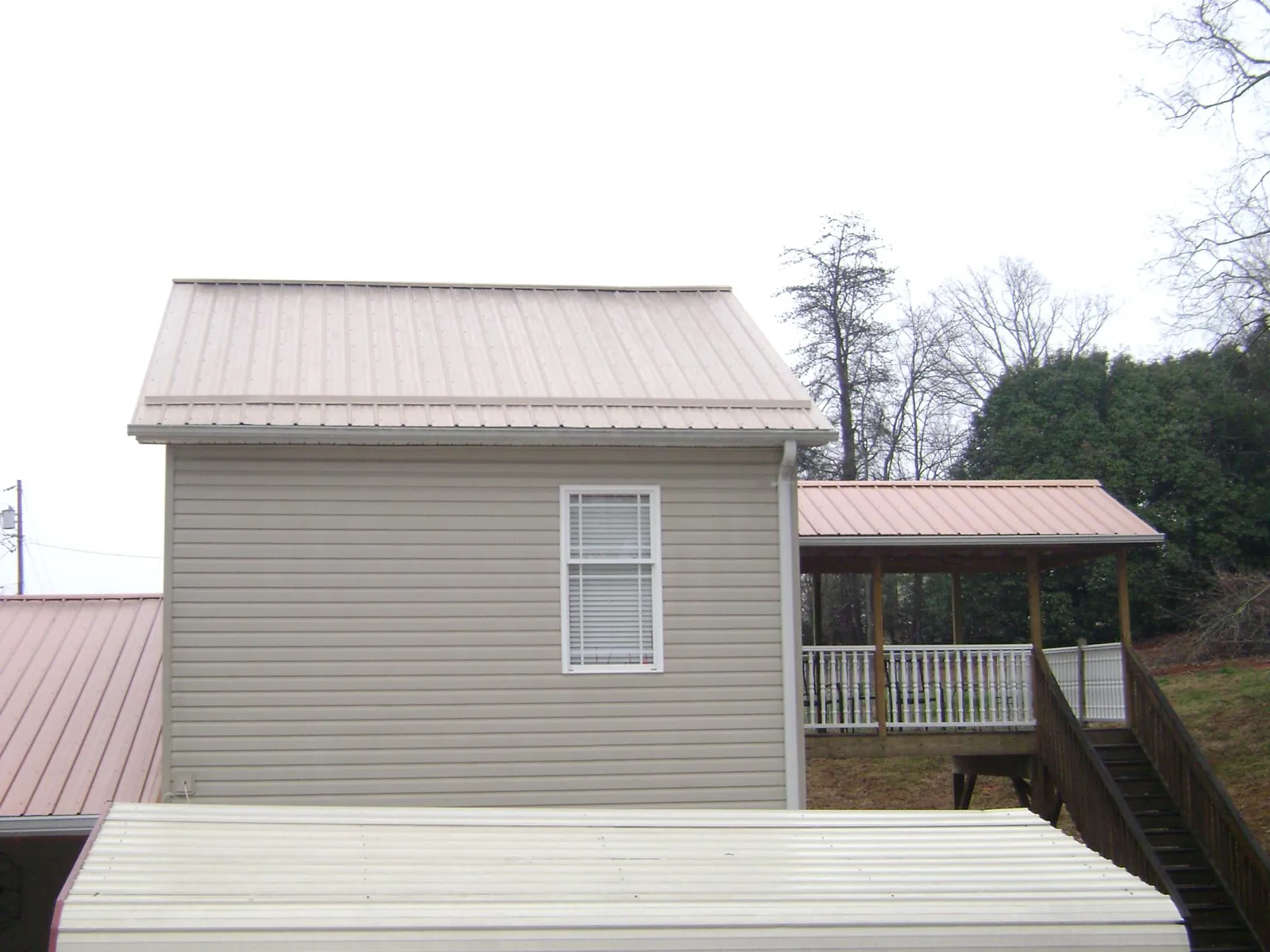 Tan metal roofs on a two story addition and attached porch, from a Roof Replacement job in Connelly